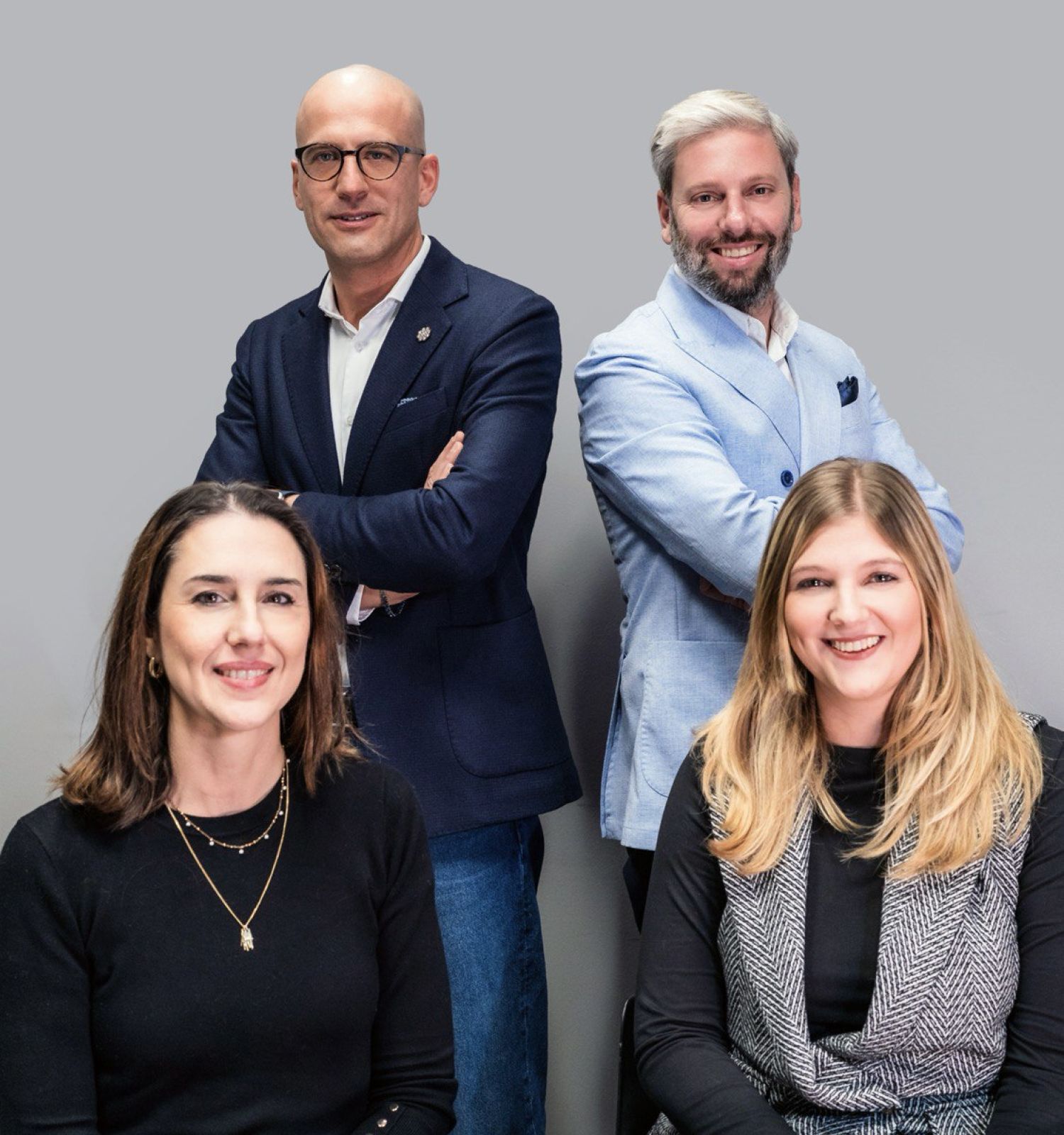 Foto di 4 persone in posa, due donne davanti sedute e due uomini dietro in piedi con sfondo grigio