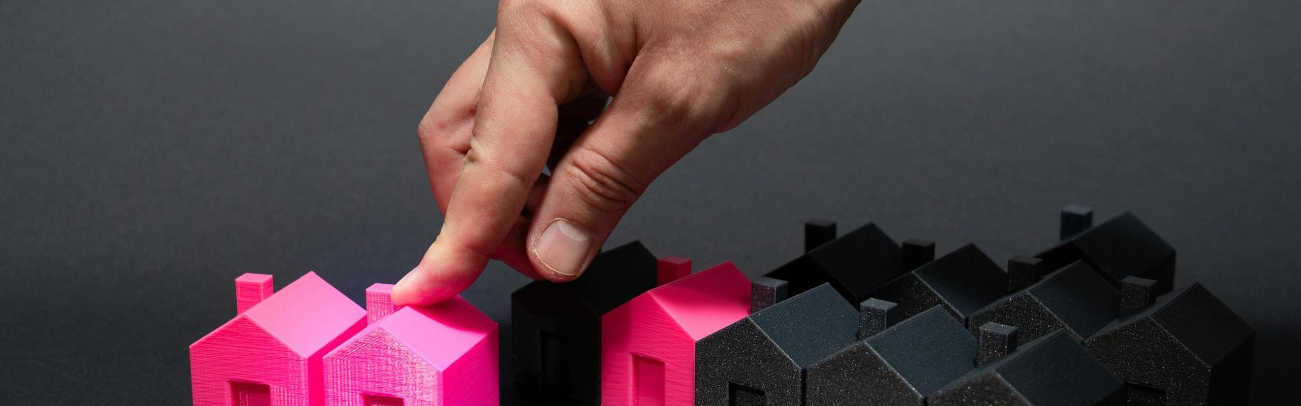 foto di casette stilizzate nere e rosa e una mano che allontana due casette rosa