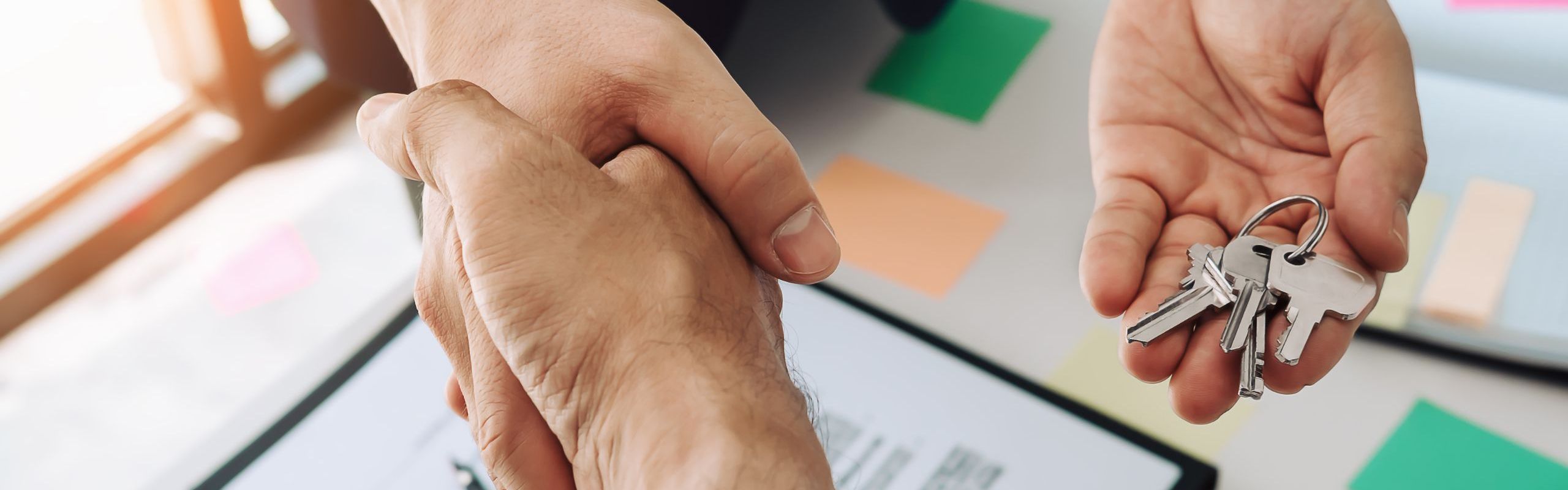 foto di due persone che si stringono la mano e una consegna delle chiavi di casa, sulla scrivania una copia di un contratto