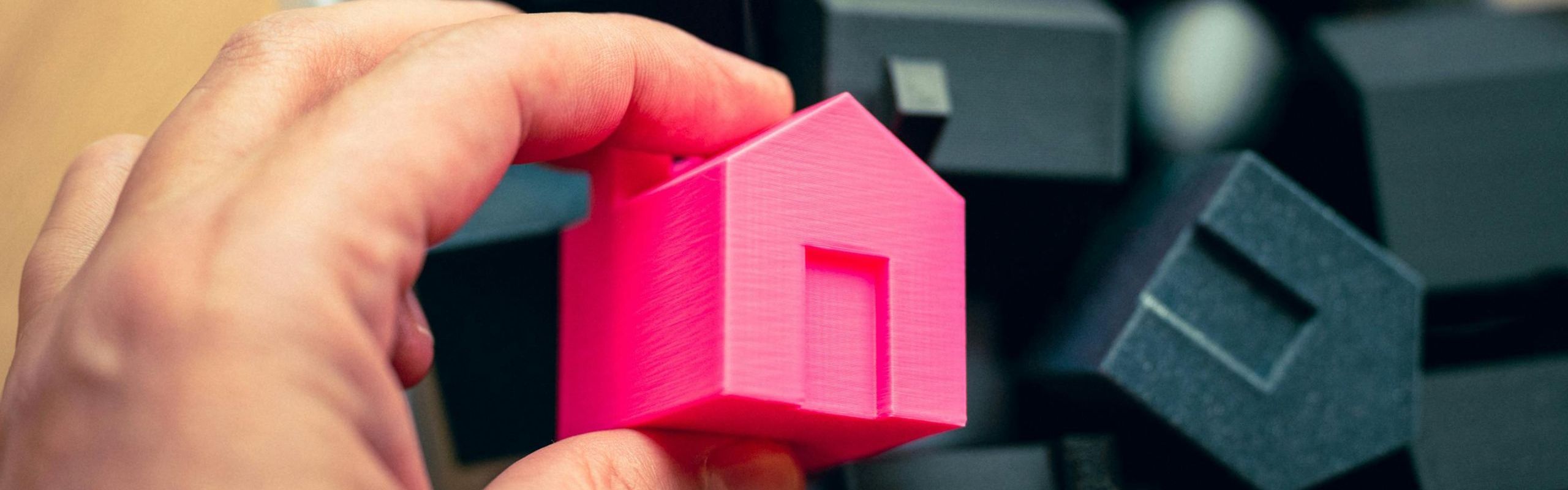 foto di Mano che afferra una casetta in miniatura rosa in mezzo ad altre case in miniatura nere